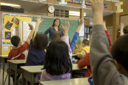 Teacher in front of classroom of students with hands raised. 